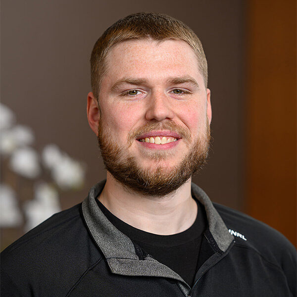 Smiling man with short hair and beard in black jacket, blurred background; About Canadian Honker Restaurant.