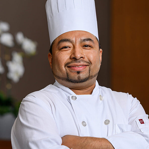 Chef in a white uniform at Canadian Honker Restaurant smiles with arms crossed in a pro setting.